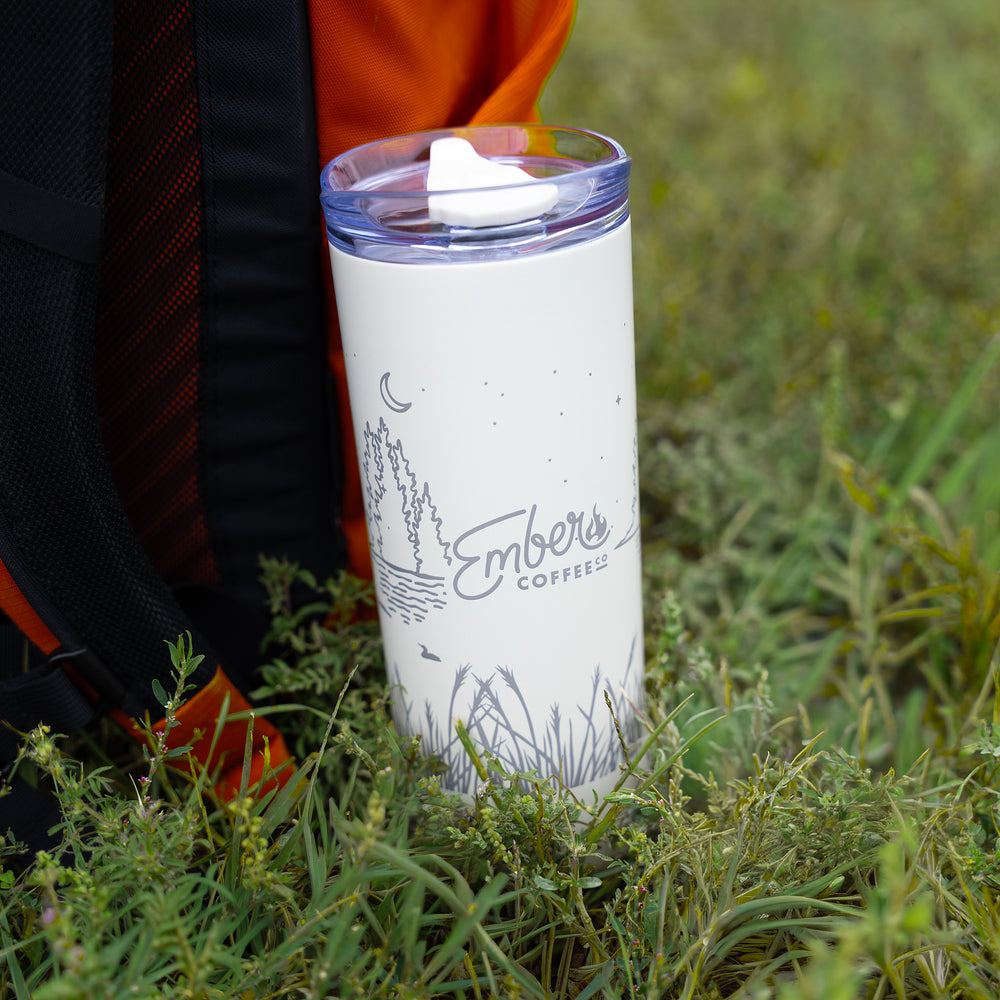 Ember Style Petal Tumbler standing in tall grass beside an orange backpack