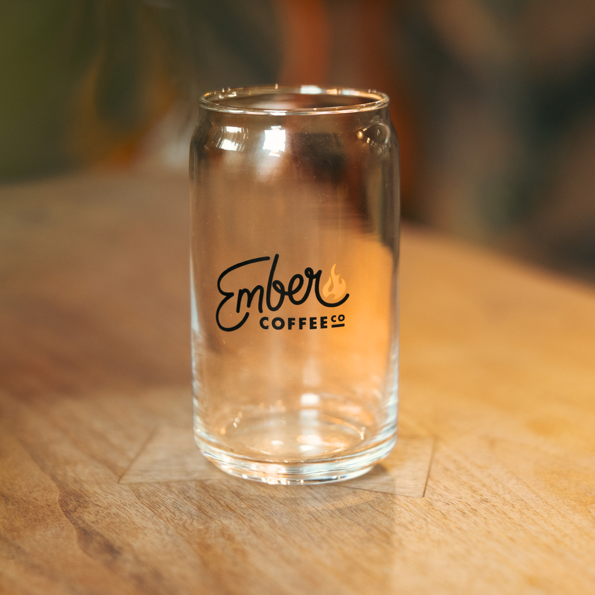 Glass Beer Can, clear glass can tumbler with Ember Coffee Co. logo, on a wood table