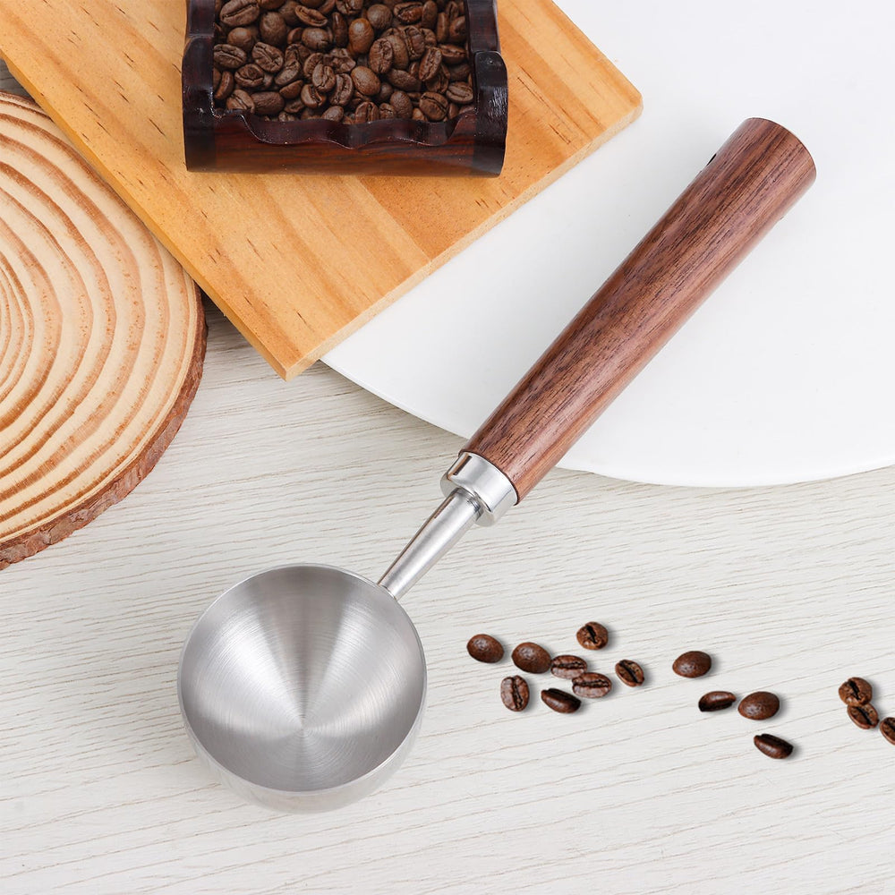 Stainless steel coffee scoop with a wood handle, beside whole coffee beans