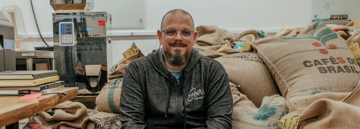 Coffee roaster standing beside stacked burlap sacks