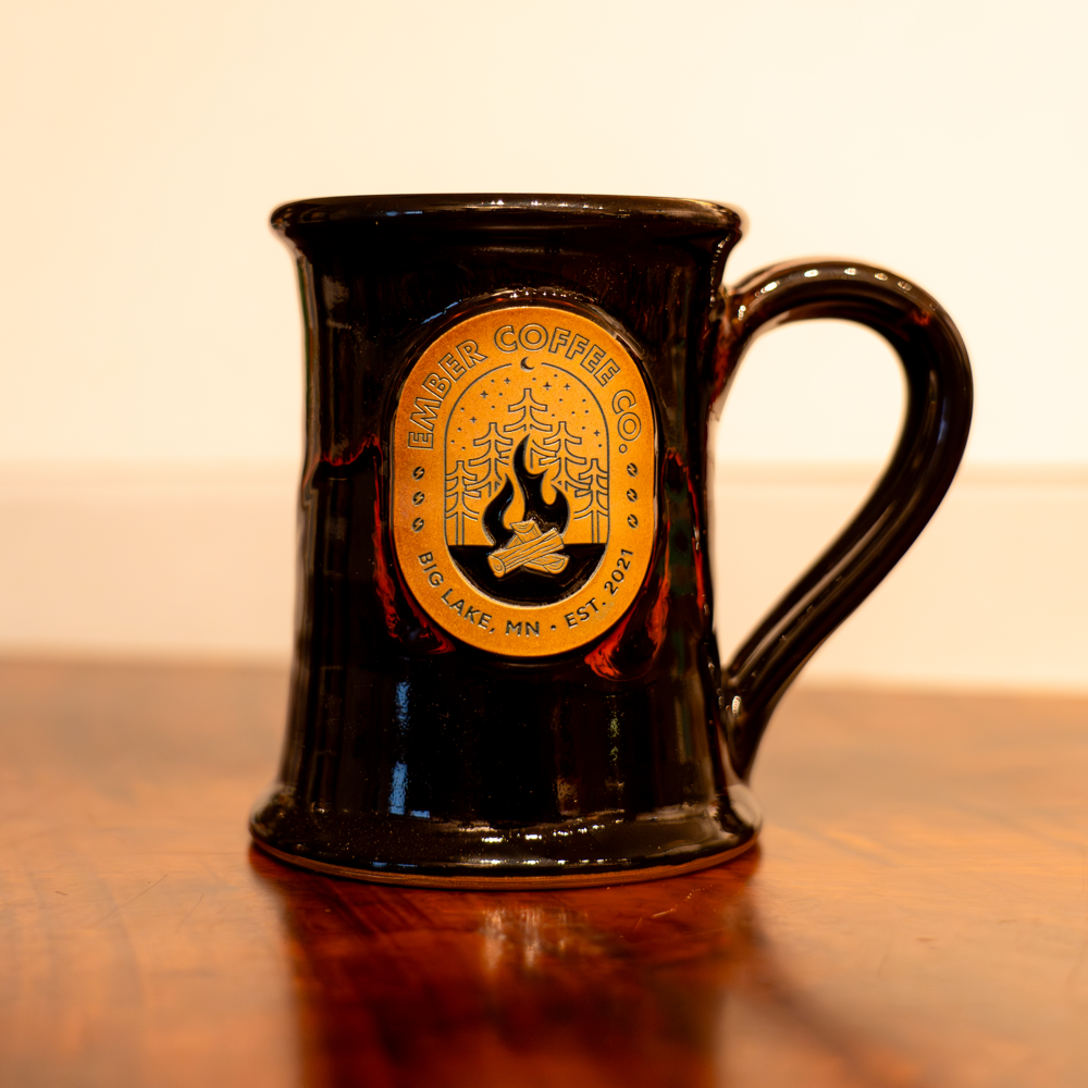 Campfire Pottery Mug, black hand-thrown pottery mug with Minnesota Campfire badge, on a wood table